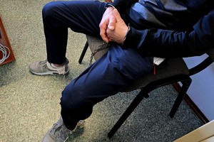 Na zdjęciu zatrzymany z założonymi kajdankami na dłonie i nogi