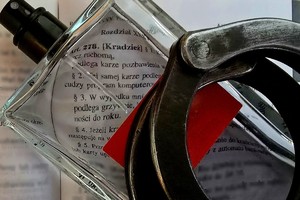 Na zdjęciu flakon perfum i kajdanki na kodeksie karnym